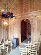 Nave of a small wooden church, showing Romanesque archway to choir and iron chandelier.