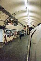 An underground station platform with curved walls and ceiling. A train is alongside the platform.