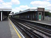 A railway track separating two railway platforms with yellow lines painted on them running parallel to the track all under a light blue sky with white clouds