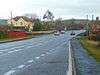 Large road w2ith houses to left and right and hills beyond.