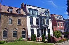 Three 19th-century brick houses attached at the sides. The one on the left is brown, the center one white and the right one red.