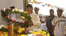 A man lays a floral wreath, surrounded by four other men