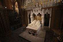 A tomb made of white stone, depicting a man and a woman with lions at their feet