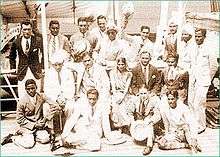 A group of Asian men wearing light coloured suits posing for the camera as a team.