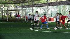 Men playing football on artificial grass pitch.