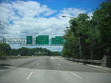 A six lane freeway in a wooded area at an interchange with three green signs over the road. The left sign reads west Interstate 280, the middle sign reads exits 4 B-A Eisenhower Parkway 1 mile, and the right sign reads exit 5A County Route 527 south Livingston with an arrow pointing to the upper right.