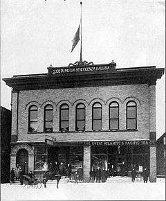 Two-story building with several people standing in front and flag on roof at half-mast