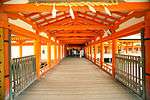 Roofed wooden corridor over water with red beams.