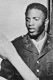 Black man in military uniform featuring the crossed-sabre insignia of a U.S. Cavalry unit receives a salute from a person out of view.