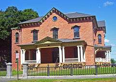 A brick house with pointed roof behind a metal fence