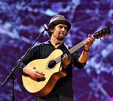 A Caucasian man wearing a bucket hat strums a guitar.