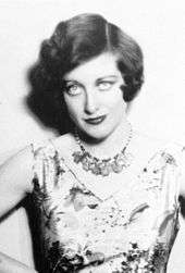 Upper body studio shot of a young Crawford in a sleeveless dress, with accented eye make-up, coiffed hair. She is staring into the camera.