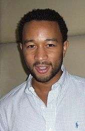 A picture of an African-American man with short back hair. He is wearing a white shirt with blue checkered lines in it.