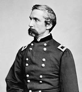 Profile of a white man with a drooping mustache wearing a double-breasted military jacket with a rectangular patch and star on each shoulder.