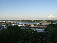 An overlook of a city in the foreground and a river running through the middle of the picture. Three bridges cross the river.