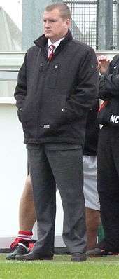 Karl Marginson, F.C. United's manager, stands at the side of a football pitch watching the game.