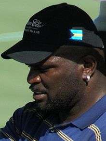 A man in a blue shirt with gray, white, and black stripes, wearing a black baseball cap.