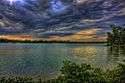 Gray storm clouds roll over green trees and plants that rim a choppy gray lake