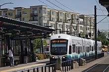 Light rail vehicle at ground level platform. Behind it is a multi-story apartment building