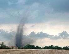 A dark tube can be seen as it pulls up dirt from the fields against a bright blue sky.