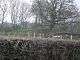 A flat topped grassy mound behind a barbed wire fence and hedgerow