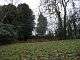 A grassy field with a wooden gate, behind which is a grassy flat topped mound, with trees around it