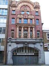 Narrow four storey red building above a wide archway