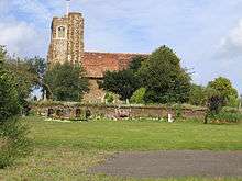 A stone church seen from the south, with a tower and stair turret to the left, and the red tiled body of the church to the right