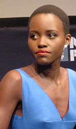 A woman seen wearing a blue dress while standing in front of a photography backdrop.