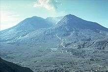 The same volcano and landscape as in the previous picture. Much of the mountain is missing, replaced by an enormous caldera (volcanic crater). The previously forested landscape is now barren as the trees were destroyed in the volcanic blast.