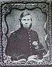 Framed portrait of a white man with a full bushy beard, wearing a dark military jacket and holding a tall feathered military hat.