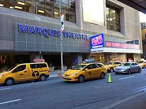 A large sign with lighted letters reading Marquis Theatre next to a theatre marquee advertising the thetre's current show