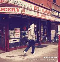 An adult Caucasian male wearing a grey hooded sweatshirt and jeans walks away from the camera in front of a deli market