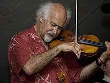 A man wearing a red printed shirt, playing the fiddle