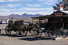 Two wagons in front of a wooden building with a surrounding patio.