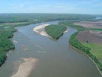 Aerial view of a brownish river winding through an agricultural valley