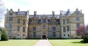 Facade of house built of yellow stone. Three floors with many large, mullioned windows and Dutch gables to the roof.