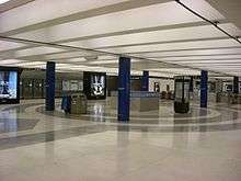 Am empty mezzanine of a train station with ticket machines and information kiosks in the background