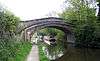 The bridge crosses the canal with a wide footpath on the left and long boats visible through the arch.