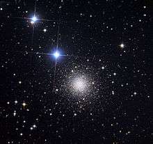 a round cluster of tiny distant stars with two bright bluish stars to the upper left