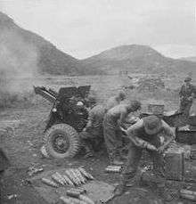 Soldiers firing a howitzer against a mountainous backdrop.