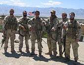 A color image of six military personnel dressed in their combat uniforms and holding weapons.