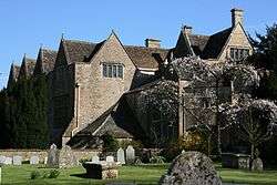 Old mansion house with traingular roofs. In the foreground is a graden with gravestones.