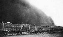 A large cloud of dust next to a farm