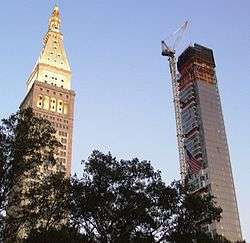 One Madison, a tall, narrow black building with squarish projections is under construction. It stands to the right of the MetLife Tower, a similarly tall building with a pointed roof.