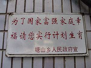 A white sign with two lines of red Chinese characters and a smaller one beneath them on a background of white tile