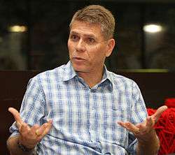 Paulo Autuori is leading a discussion. He is an older man wearing a buttoned-up shirt with sky blue figures on a white background.