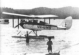 Single-engined biplane on floats, parked on the water with two boys in foreground