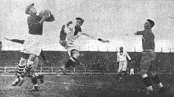 An action shot from a football match. A goalkeeper jumps and catches the ball.