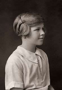 Head-and-shoulders black and white photograph of a young girl. She wears a light-coloured blouse and faces right, looking out of the picture, with a slight smile. Her short hair is pulled back from her face and pinned up.